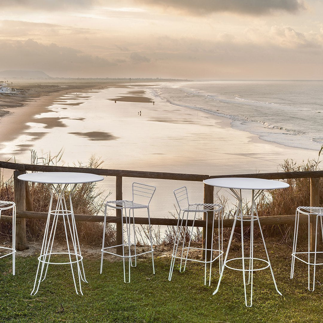 White wire bar stools and tables set against a serene beach sunset backdrop, featuring soft earth tones and gentle waves.