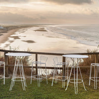 White wire bar stools and tables set against a serene beach sunset backdrop, featuring soft earth tones and gentle waves.