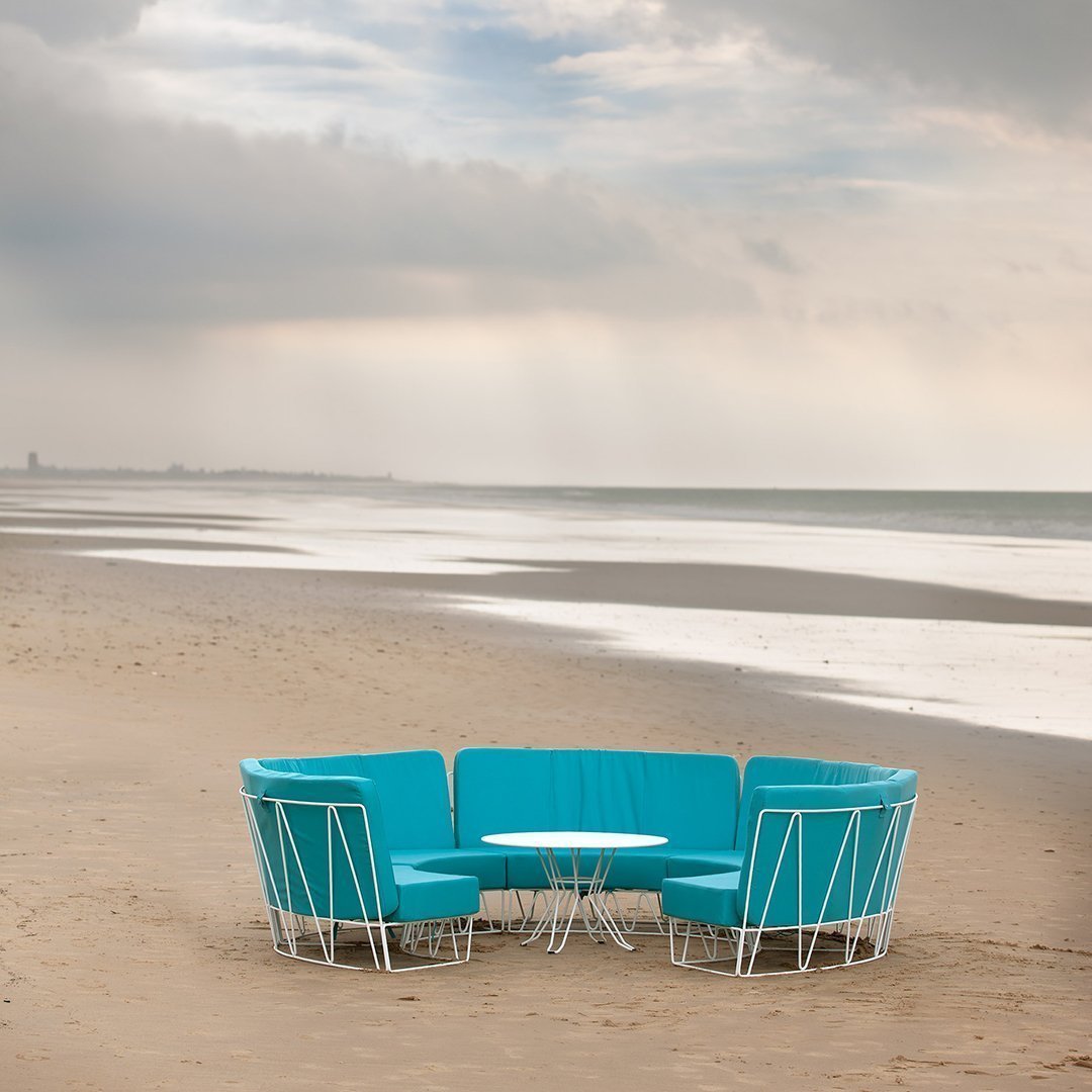 Turquoise outdoor seating set with circular arrangement and white accents, placed on a sandy beach.