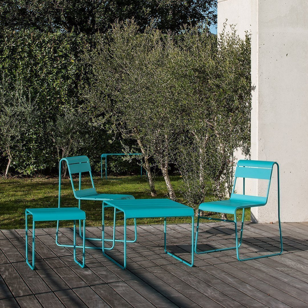 Turquoise metal outdoor chairs and table with a minimalist design, set against a natural green backdrop.