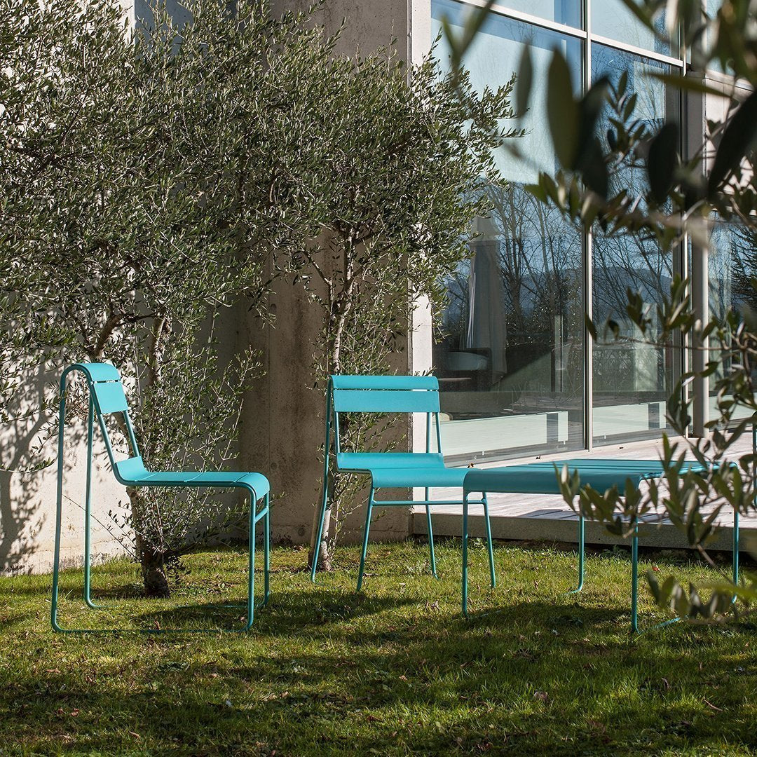 Turquoise outdoor chairs and table against a backdrop of green grass and olive trees, showcasing modern simplicity.