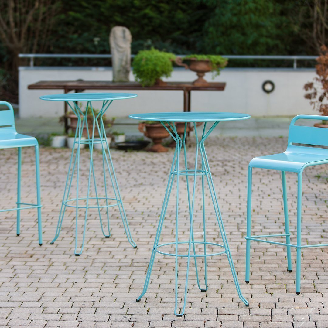 Turquoise metal bistro table and chairs set against a textured stone patio, perfect for outdoor dining.