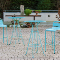 Turquoise metal bistro table and chairs set against a textured stone patio, perfect for outdoor dining.