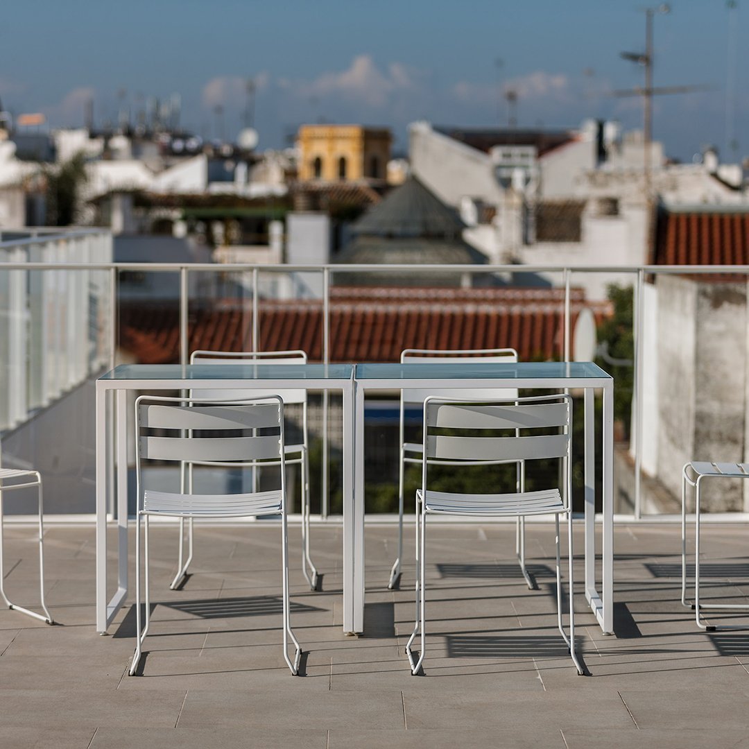 White metal table and chairs set against a backdrop of urban rooftops, featuring a sleek, minimalist design.