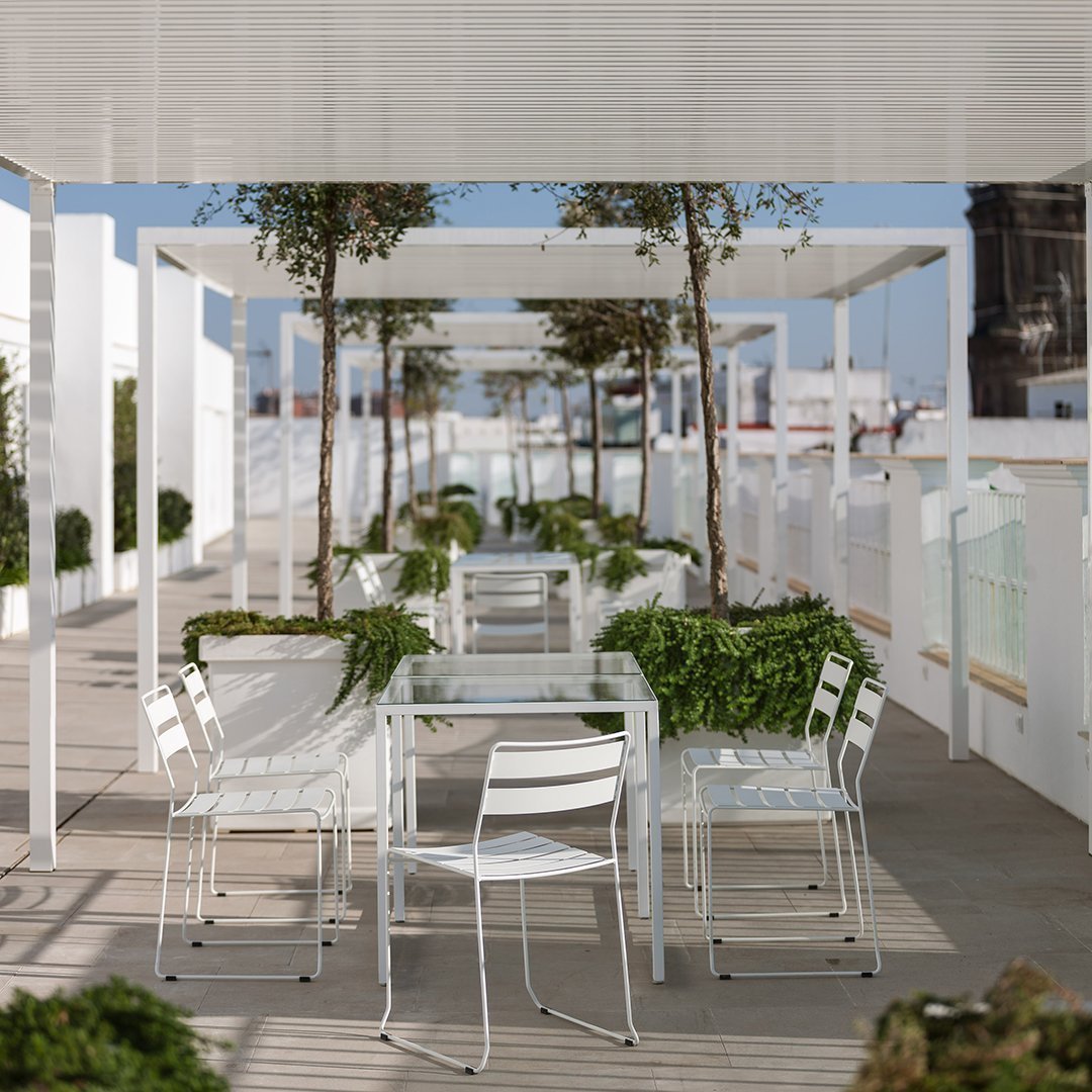 Modern outdoor dining area with white furniture and green planters, featuring a bright, open, and airy design.
