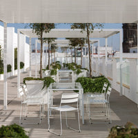 Modern outdoor dining area with white furniture and green planters, featuring a bright, open, and airy design.
