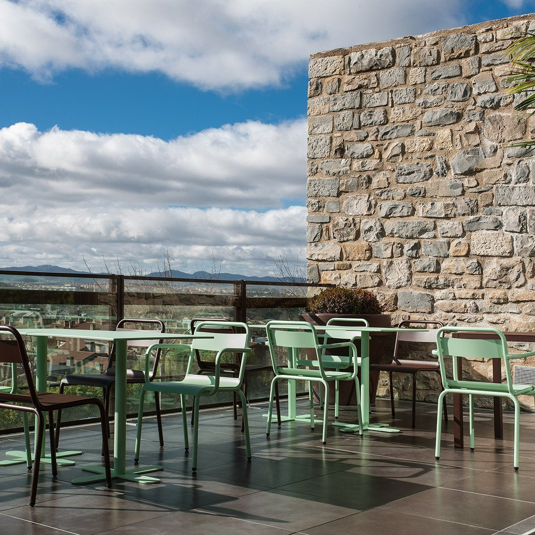 Stylish mint green chairs and tables against a stone wall, with a scenic view under a clear blue sky.