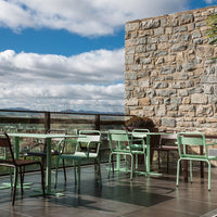 Stylish mint green chairs and tables against a stone wall, with a scenic view under a clear blue sky.