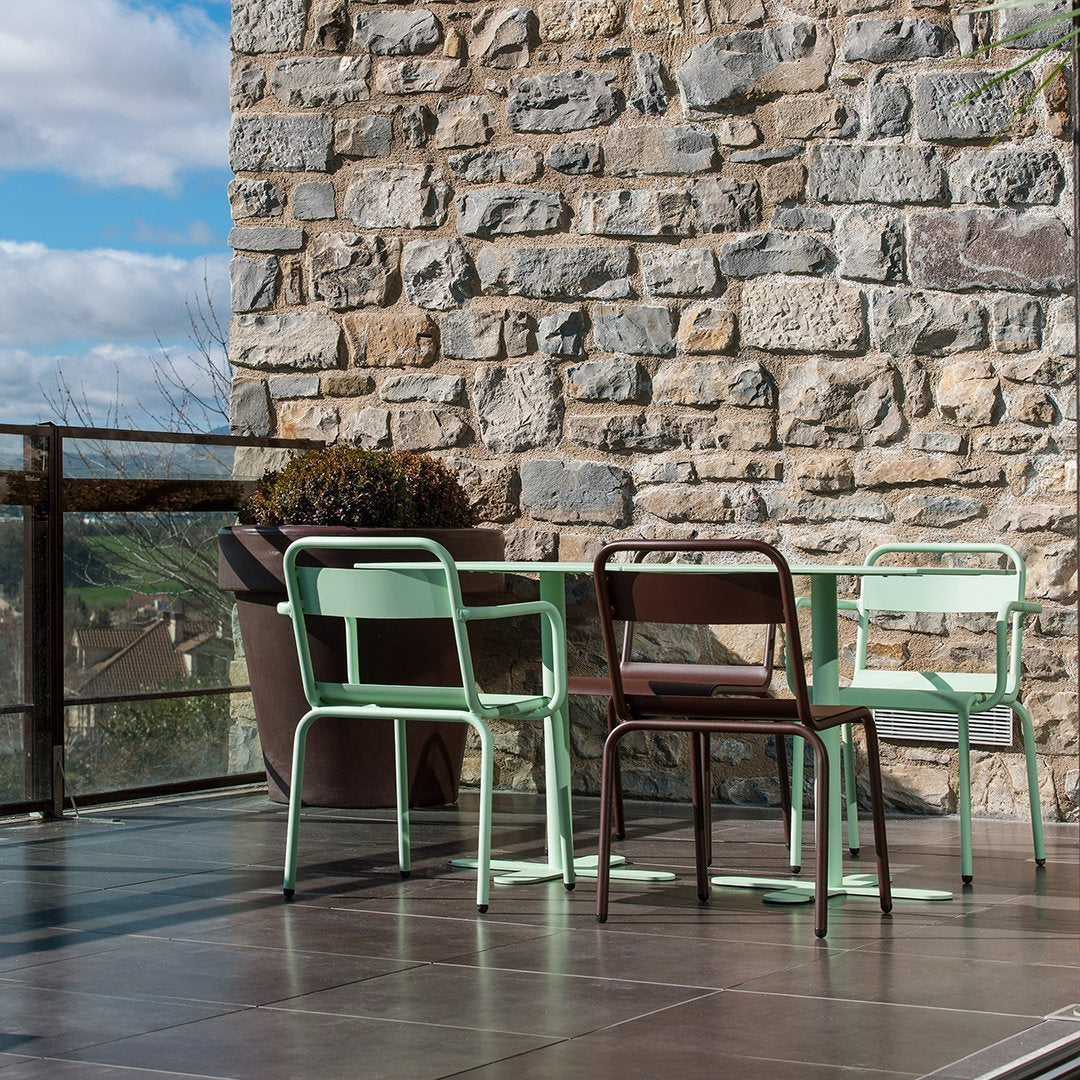 Mint green and brown metal chairs arranged around a table, contrasting against a textured stone wall.