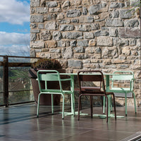Mint green and brown metal chairs arranged around a table, contrasting against a textured stone wall.