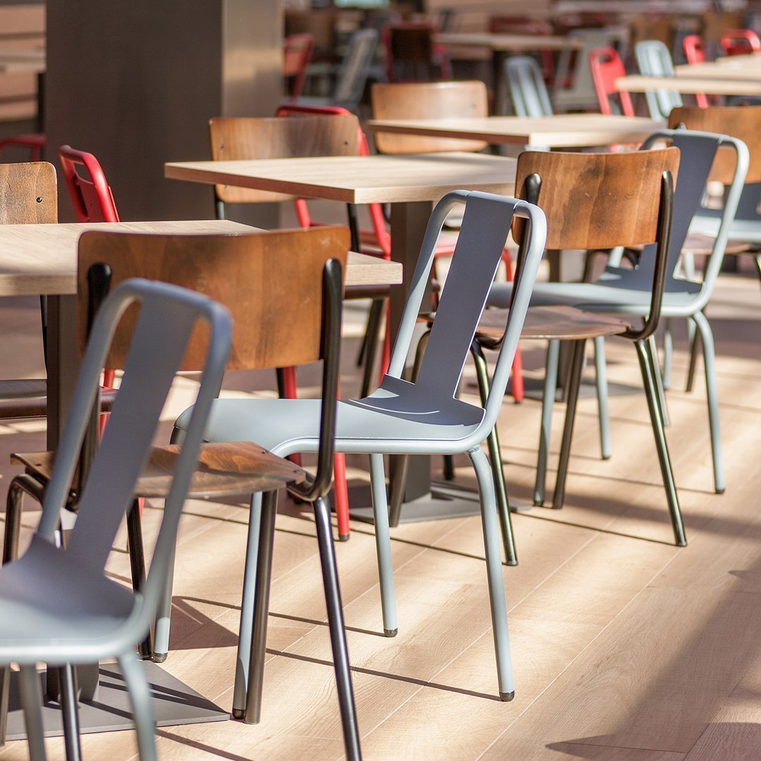 Colorful chairs in muted tones of blue, brown, and red arranged around light wood tables in a contemporary setting.