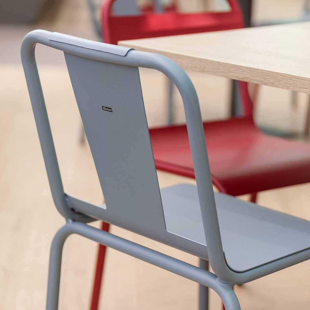 Gray metal chair with a sleek design, featuring a contrasting red chair in the background, perfect for modern spaces.
