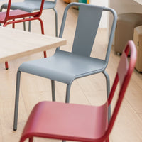 Gray metal chair with a sleek design, alongside vibrant red chairs, creating a modern aesthetic in a bright space.