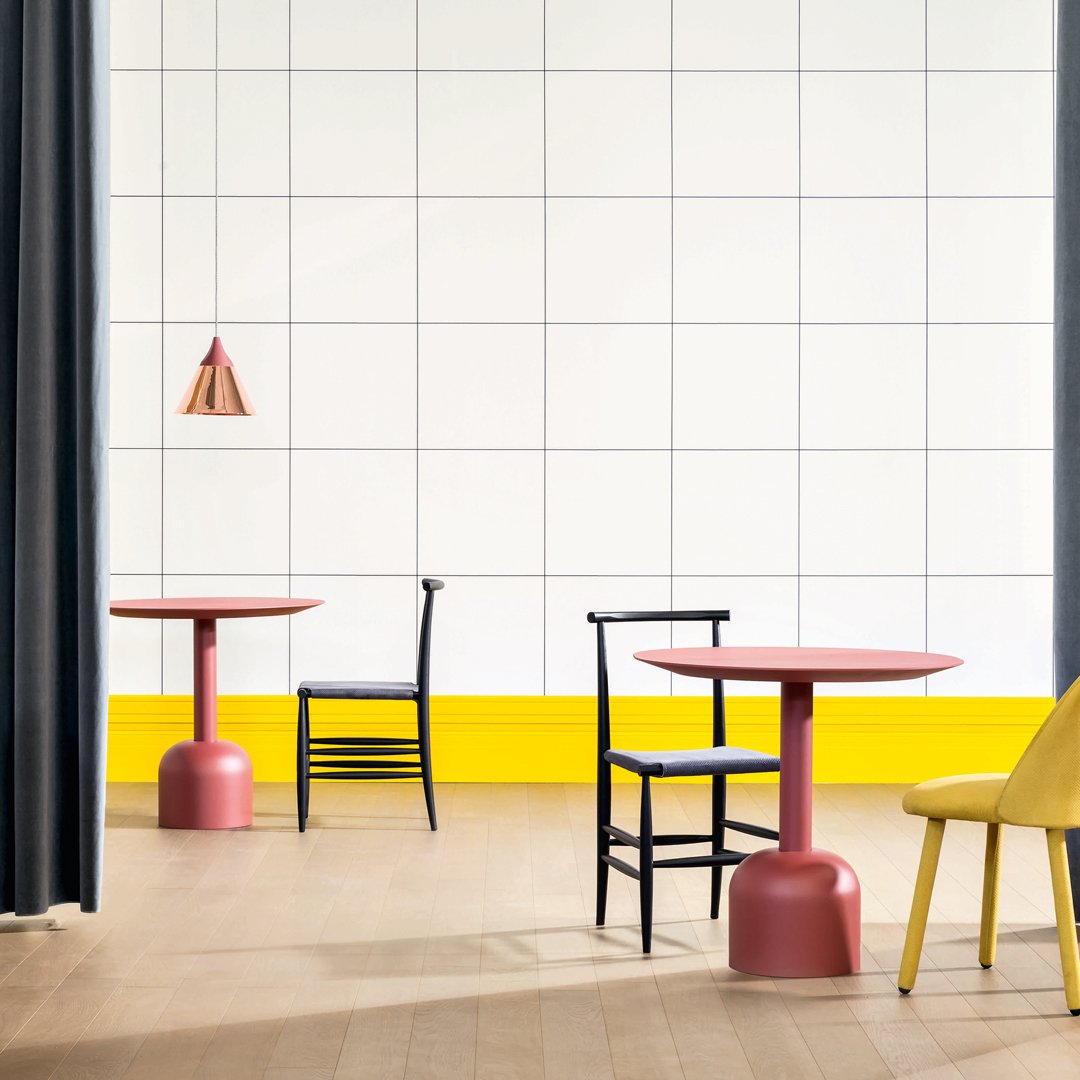 Two modern tables in pink and black with yellow accents; minimalist design against a grid-pattern wall.