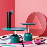 Teal and pink geometric decor featuring round tables, a black sculpture, and a colorful patterned rug.