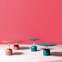 "Modern coffee tables in teal and pink against a coral background, featuring sleek round tops and unique bases."