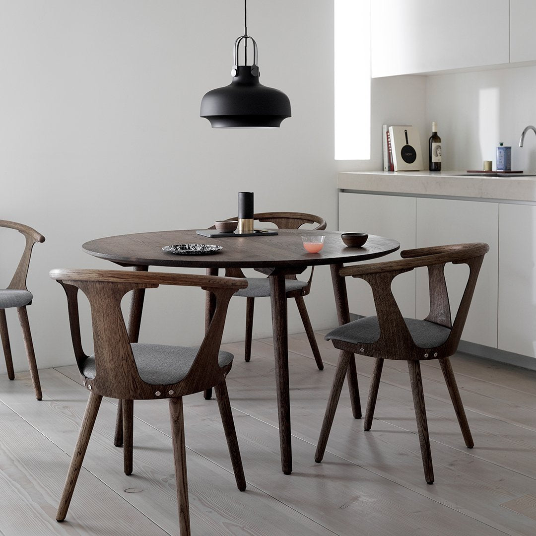 Round wooden dining table with dark brown finish, paired with gray upholstered chairs and a sleek black pendant light.