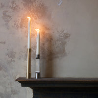 Elegant white candles in sleek gold and silver holders against a textured beige wall, creating a warm ambiance.