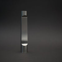 Sleek, vertical silver metal sculpture with smooth, reflective surface against a dark background.