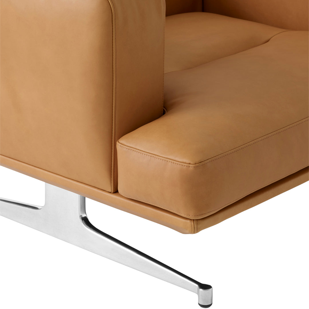 Tan leather sofa corner with smooth, minimalist design and sleek chrome legs.