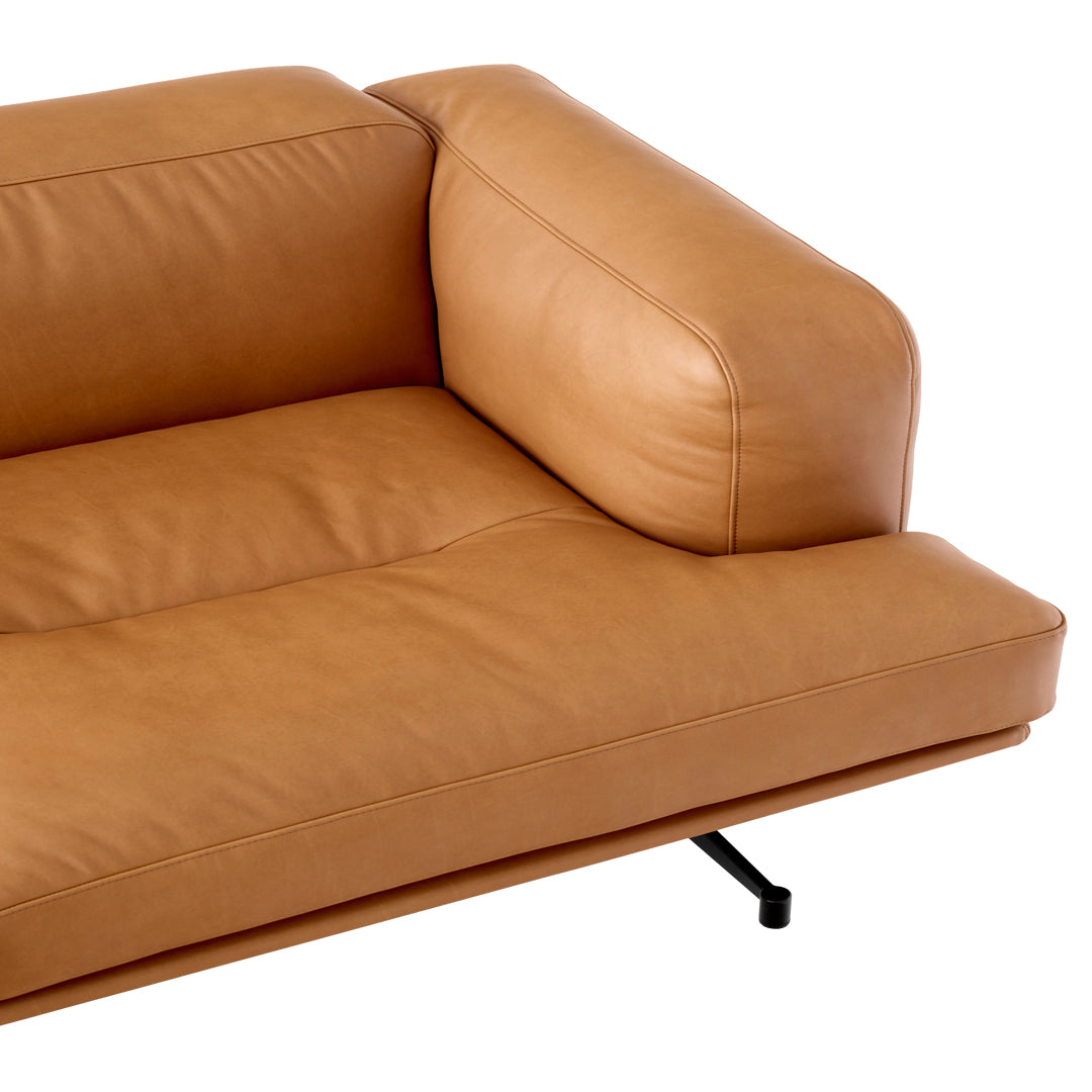Tan leather couch with a smooth surface and minimalistic design, featuring a sleek black metal base.