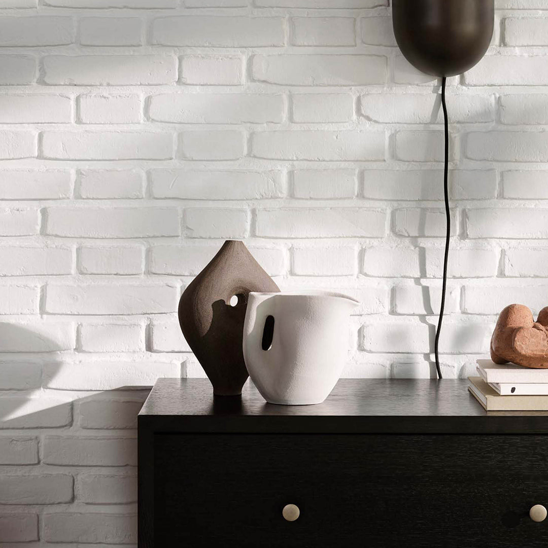 Brown and white ceramic vases with unique shapes, set against a textured white brick wall.