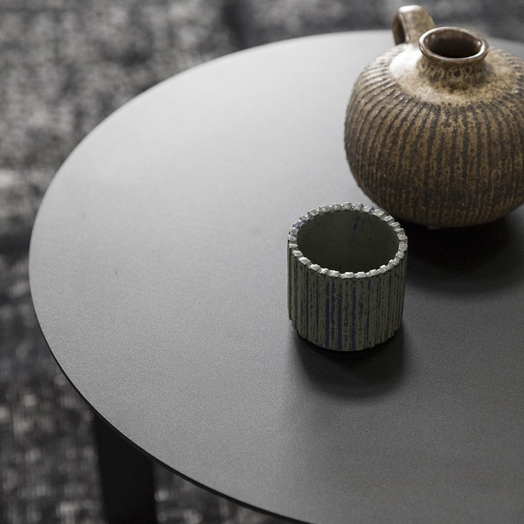 Minimalist black table with textured brown vase and striped green candle holder, showcasing earthy tones and modern patterns.
