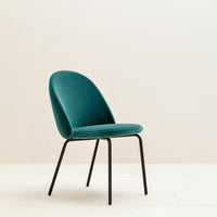 Teal velvet chair with a smooth, rounded design and sleek black legs against a neutral backdrop.