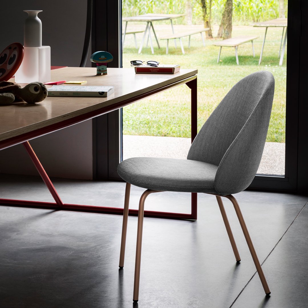 Gray upholstered chair with smooth, curved lines and slender metal legs, set against a modern minimalist desk.