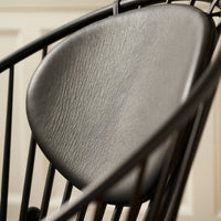 Black woven chair with a sleek leather seat, featuring a minimalist design and elegant curves. Perfect for modern decor.