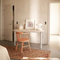 Light wood desk, pastel peach chair, beige patterned rug, and soft gray walls create a warm, modern aesthetic.