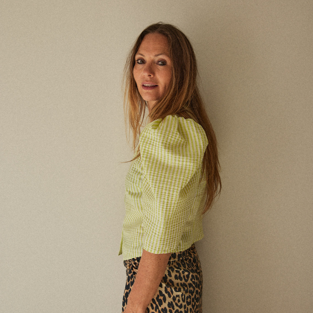 Julie Sauvage wearing a green checkered shirt and leopard print pants against a plain wall.