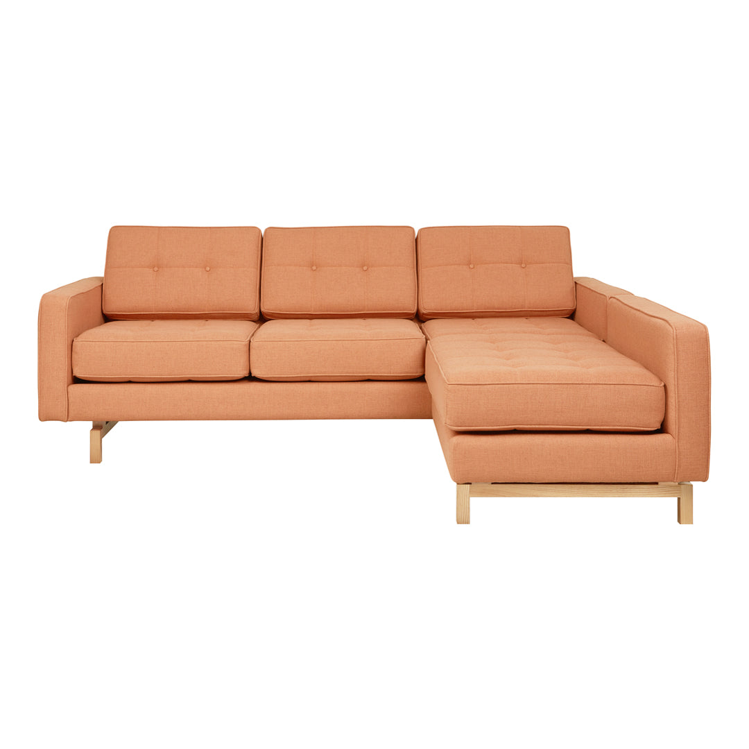 Modern peach-colored sectional sofa with a tufted design and light wooden legs, ideal for contemporary interiors.