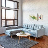 Light gray sectional sofa with tufted upholstery, complemented by a textured dark gray area rug and wooden coffee table.