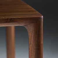 Close-up of rich brown wooden table leg with smooth curves and a natural grain pattern against a dark background.