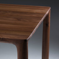 Close-up of a smooth, dark walnut wooden table with a natural finish and rounded edges. Elegant and minimalistic design.
