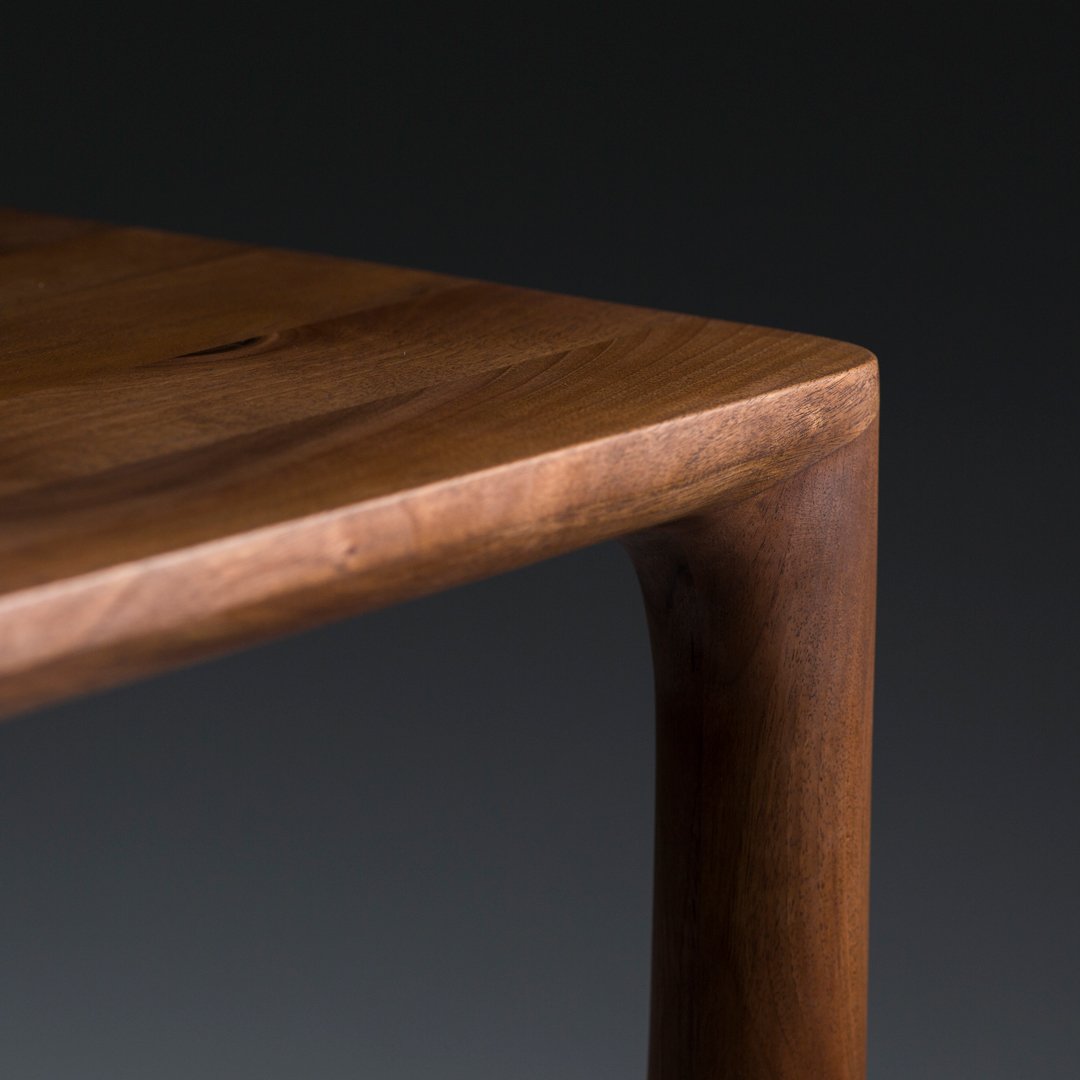 Close-up of a smooth, warm-toned wooden table corner with a sleek, natural finish and rounded edges, highlighting grain patterns.