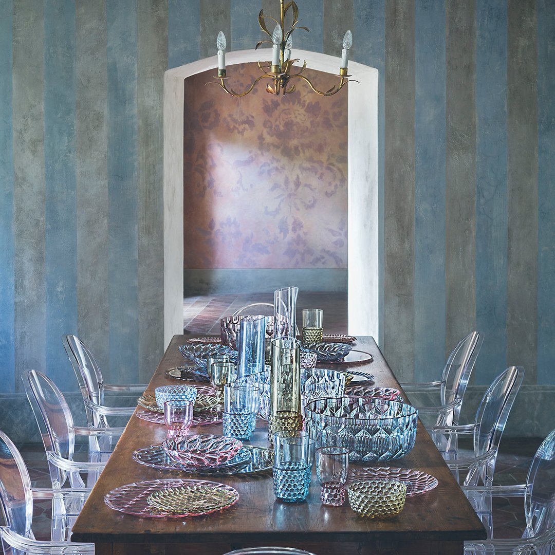 Elegant dining table set with pastel blue and pink patterned plates, glassware, and a textured wall background.