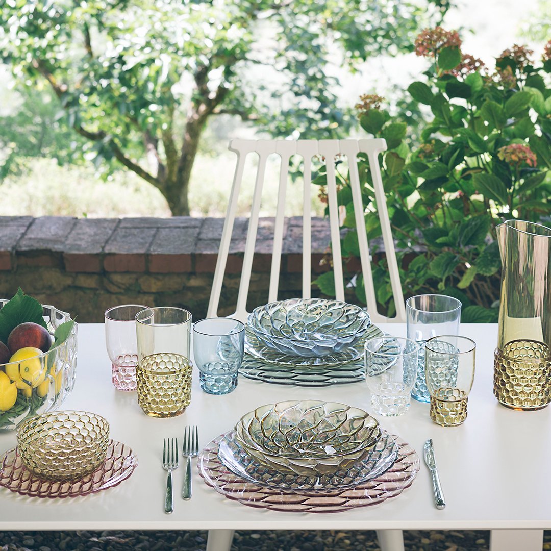 Colorful tableware set with textured glass plates and vibrant drinkware in shades of blue, green, and pink.
