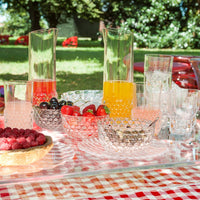"Colorful glass pitchers and bowls on a red checkered tablecloth, featuring vibrant fruits and refreshing drinks."