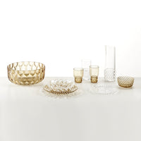 "Gold and clear textured glass dinnerware set featuring bowls, plates, and glasses with intricate geometric patterns."