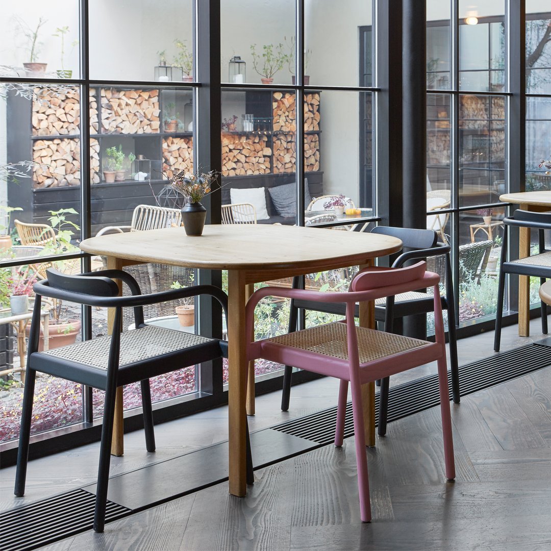 "Modern wooden table with two chairs: one black and one pink, set against a bright, airy backdrop."