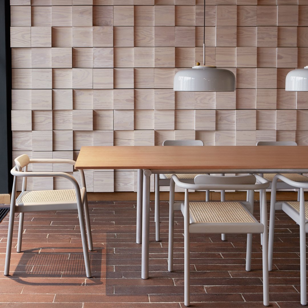 Light wood wall with textured panels, natural wood table, and neutral-toned chairs create a warm, inviting atmosphere.