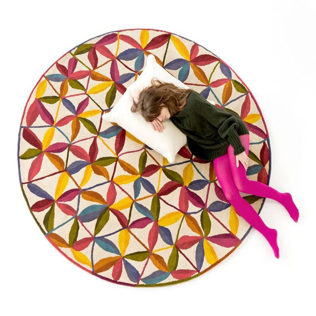 Colorful round rug featuring a vibrant geometric pattern with petals in shades of red, yellow, blue, and green.