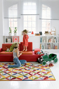 Colorful geometric patterned rug featuring red, yellow, blue, green, and white accents, enhancing a bright living space.