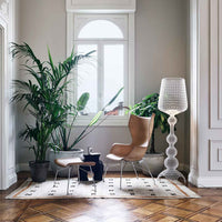 Stylish brown chair, white patterned rug, and green plants in a bright, airy room with wooden floors and soft gray walls.