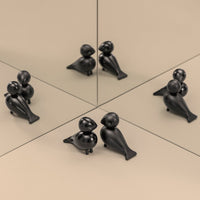 Black decorative figurines with smooth finishes and playful shapes, set against a beige background and mirrored surfaces.