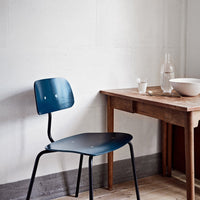 Dark blue metal chair with minimalist design next to a wooden table in a light, neutral-colored setting.