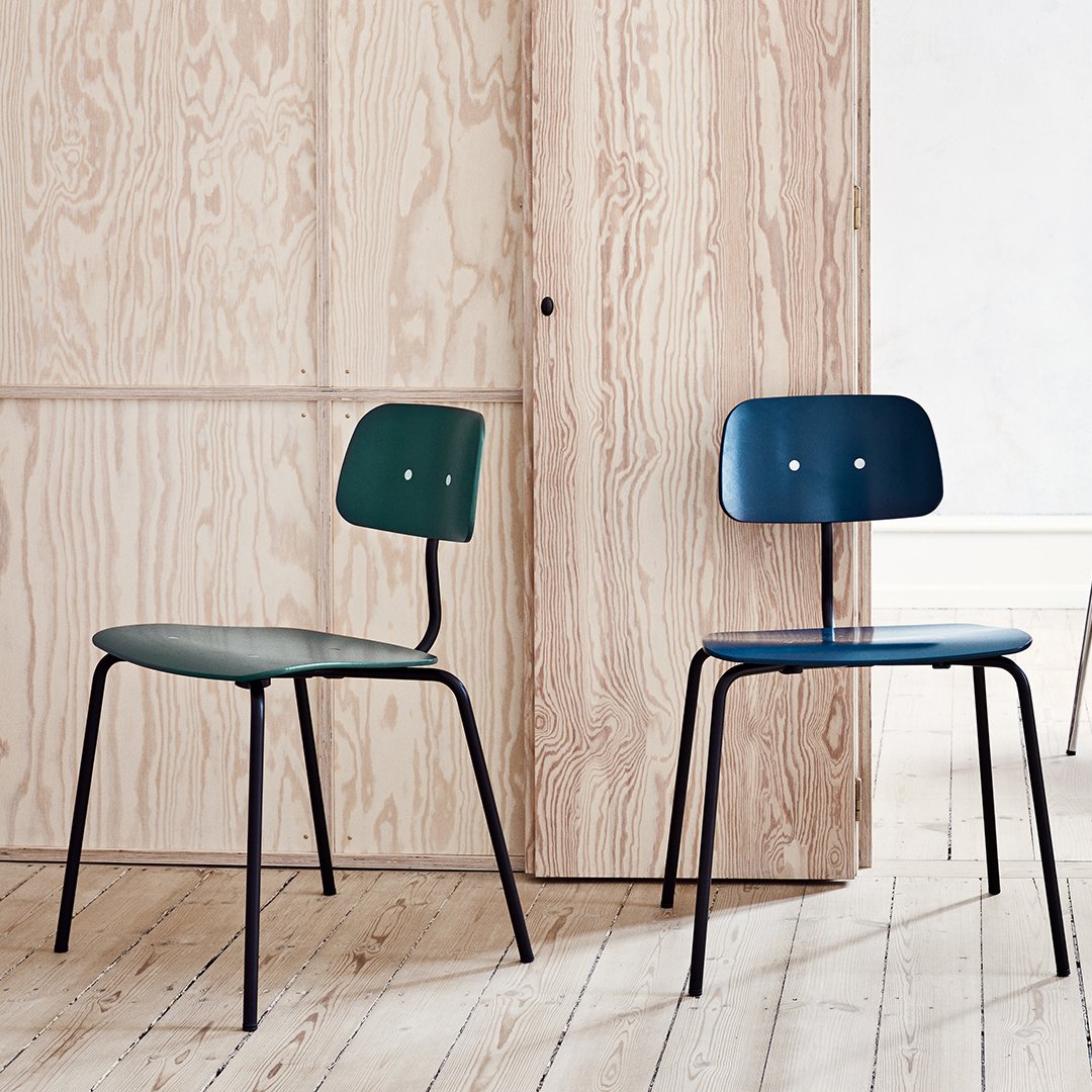 Two minimalist chairs in dark green and navy blue, featuring smooth surfaces and subtle shapes against a light wood backdrop.