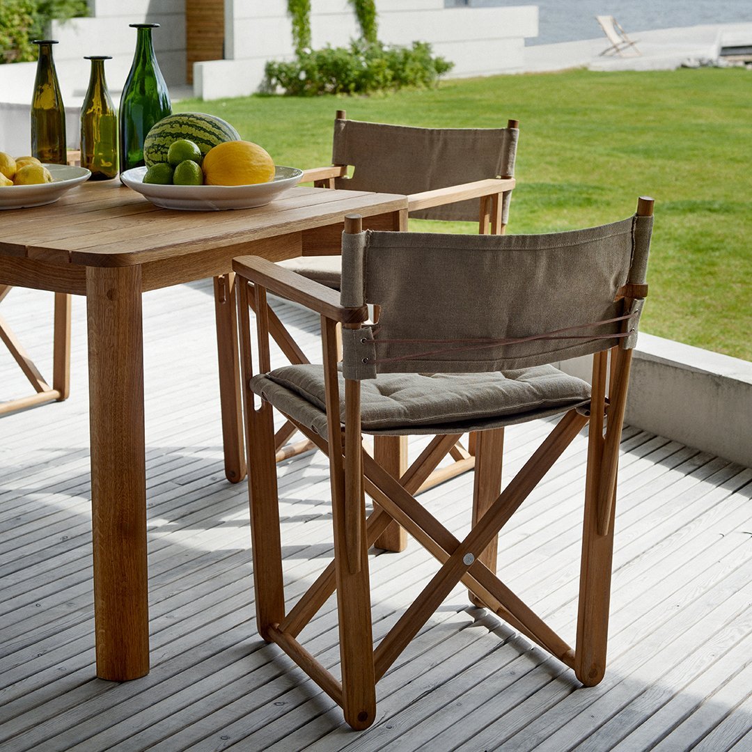 Natural wood table with light gray fabric chairs, set against a green lawn and contemporary outdoor decor.
